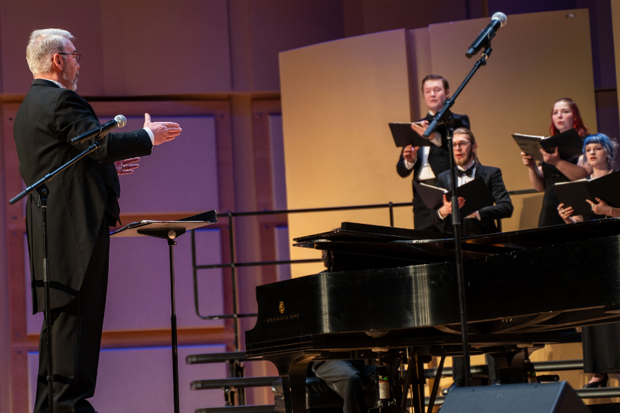 Dr. Anderson conducts a choir on the Jensen stage. He is wearing a black tux.